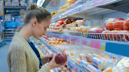 Woman buying sausage at grocery store. Consumerism, sale and shopping conceptの写真素材