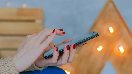 Woman using vertical black slim smartphone at home. Bokeh light background. Entertainment and...