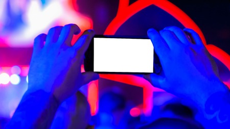 Unrecognizable hand silhouette holding smartphone with white blank display at concert. Mock up, template, entertainment and technology conceptの写真素材