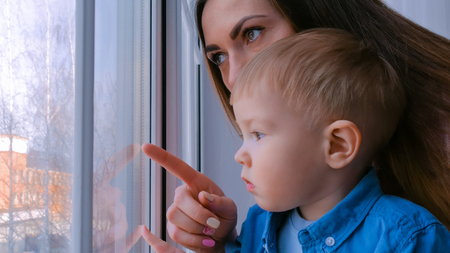Young mother and pensive little boy looking through window. Childhood and leisure conceptの写真素材