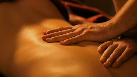 Close-up shot - masseur hands doing back massage in spa center, studio. Warm romantic illumination, low key. Wellness, relaxation and healthcare conceptの写真素材