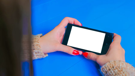 Woman looking at horizontal smartphone with white empty display. Close up shot of woman hands with...
