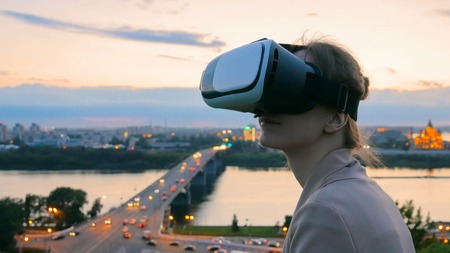Woman uses virtual reality glasses in the city after sunset. Evening time, twilight. Relax, entertainment and technology conceptの写真素材