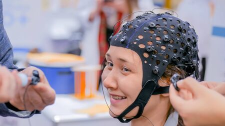 MOSCOW, RUSSIA - OCTOBER 12, 2018: Science Festival - smiling teenager girl with medical eeg headset equipment at technology exhibition. Medicine, neurology and electroencephalography conceptのeditorial素材