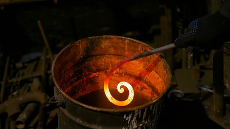 Professional blacksmith working with metal - quenching hot iron part of forged gate in water at forge, workshop. Handmade, craftsmanship and blacksmithing conceptの写真素材