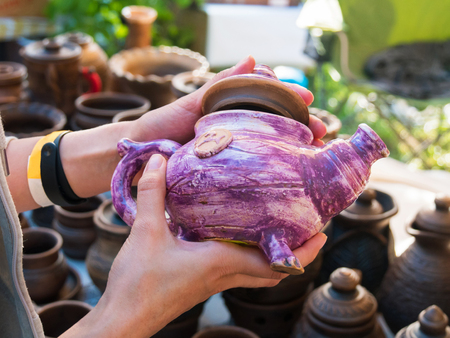 Close up of woman hands with purple handmade ceramic kettle at art souvenir market. Handicraft, creative and artwork conceptの写真素材