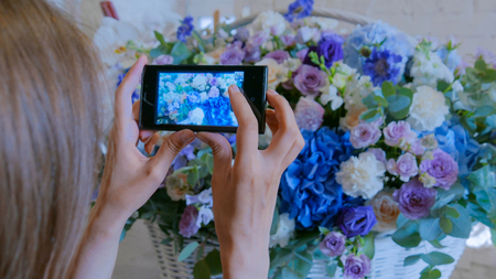 Professional floral artist, florist using smartphone and taking photo of her large floral basket with flowers at workshop, flower shop. Photography, technology and social media conceptの写真素材