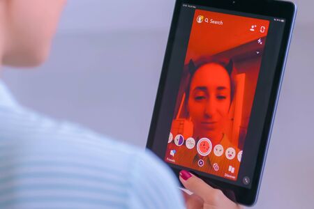 MOSCOW, RUSSIA - MAY 24, 2019: Woman using Snapchat multimedia messaging app with 3d face mask filter on tablet at home. Face detection technology, AR, social media, selfie, entertainment conceptのeditorial素材