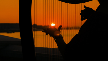 Close up shot - woman hands playing harp on city embankment at sunset. Music, leisure and culture conceptの写真素材