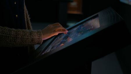 Woman using interactive touchscreen display in modern historical museum. Evening time, lowlight. Education and entertainment concept. Close up shotの写真素材