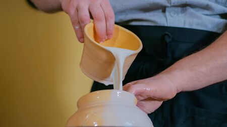 Professional male potter preparing ceramic wares for burning in pottery kiln with milk - old russian pottery tradition. Crafting, artwork and handmade conceptの写真素材
