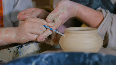 Pottery class and workshop: professional male potter working with kid and showing how to make...