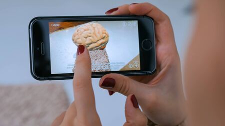 MOSCOW, RUSSIA - AUGUST 29, 2018. Woman using smartphone with augmented reality app and exploring virtual model of brain. Future, medicine and technology conceptのeditorial素材
