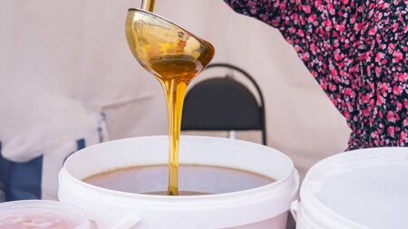Woman pouring sweet honey from the ladle at street farmers marketの写真素材