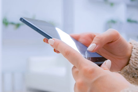 Woman hands using black smartphone with touchscreen display in white room or office - scrolling and...