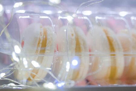 Tasty french macaroons with Christmas bokeh garland light in plastic box on table. French cuisine, candy, holiday, new year and food conceptの写真素材
