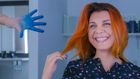 Portrait of pretty young woman with orange hair color smiling, looking at reflection in mirror and fixing hair. Beauty, fashion and make up conceptの写真素材