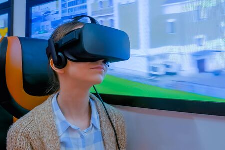 MOSCOW, RUSSIA - JUNE 25, 2019: VR Expo. Woman using black virtual reality headset, looking around and playing in passenger of public transport simulator at exhibition. Future and video game conceptのeditorial素材