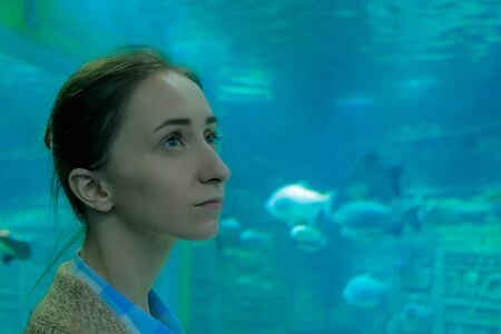 Underwater life, tourism, education and entertainment concept. Portrait of woman looking at fish in large public aquarium tank at Oceanariumの写真素材