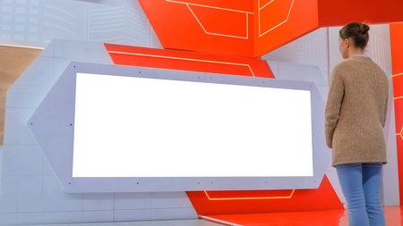 Woman looking at blank large wide interactive wall white display at modern technology exhibition or...