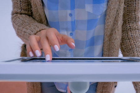 Woman hand using touchscreen display of interactive floor standing white tablet kiosk at exhibition...