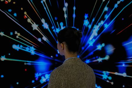 MOSCOW, RUSSIA - JUNE 01, 2019: Woman standing in front of large interactive display with colorful abstact video at modern immersive exhibition. Education, digital art and entertainment conceptのeditorial素材