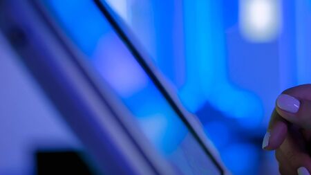 Side close up view, woman hand using touchscreen display of floor standing tablet kiosk at modern technology exhibition or museum with futuristic sci-fi interior and purple lightの写真素材