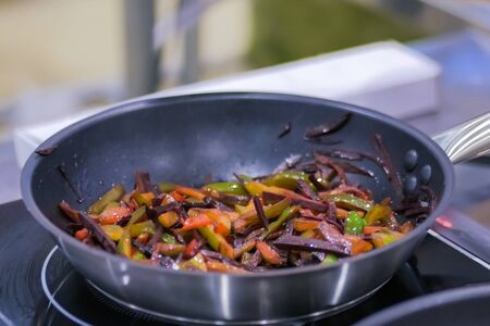 Process of cooking sliced pepper and beetroot in frying pan with oil on electric stove. Professional cooking, catering, cookery, gastronomy and food conceptの写真素材