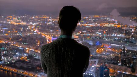 Pensive woman silhouette looking at night cityscape. View throw window of skyscraper on street with light bokeh illumination at evening. Success, opportunity and future conceptの写真素材