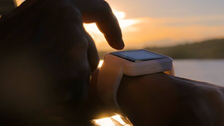 Woman using wearable smartwatch computer device on deck of cruise ship at sunset. Sunset light, golden hour. Relax, nature and technology conceptの写真素材