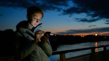 Woman using vertical smart phone on deck of cruise ship at night. Relax, technology and journey conceptの写真素材