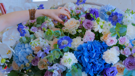Professional woman floral artist, florist making large floral basket with flowers at workshop,...
