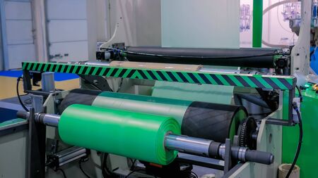 Part of automatic plastic bag making machine - moving roller with flat polyethylene green film at exhibition, trade show. Manufacturing, recycling, industry and automated technology equipment conceptの写真素材