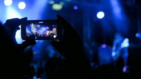 Unrecognizable hand silhouette taking photo or recording video of live music concert with smartphone. Photography, entertainment and technology conceptの写真素材