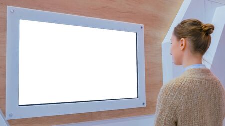 Woman looking at blank digital interactive white display wall at exhibition, museum with futuristic interior. Mock up, sci-fi, future, copyspace, template, isolated, white screen, technology conceptの写真素材