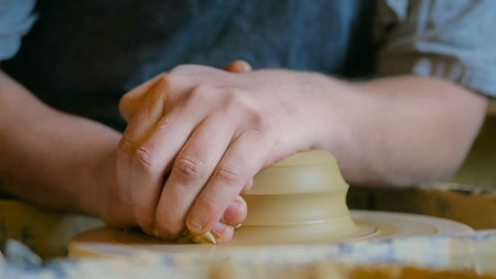 Professional male potter working with clay on potter's wheel in workshop, studio. Handmade, art and...