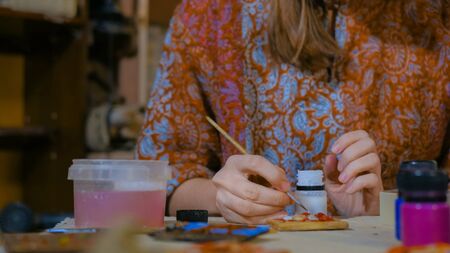 Professional woman potter, decorator painting ceramic souvenir refrigerator magnet in pottery workshop, studio. Crafting, artwork and handmade conceptの写真素材