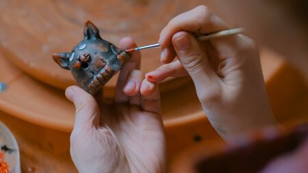 Professional woman potter, decorator painting ceramic souvenir penny whistle toy cat in pottery workshop, studio. Crafting, artwork and handmade conceptの写真素材