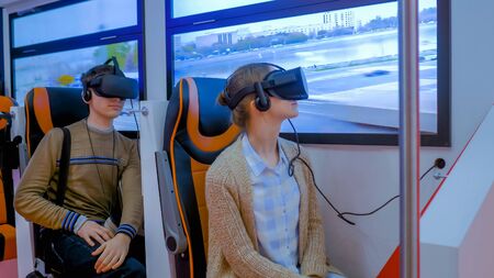 MOSCOW, RUSSIA - JUNE 25, 2019: VR Expo. Woman and man using black virtual reality headset and playing in passenger of public transport simulator at exhibition. Future and video game conceptのeditorial素材