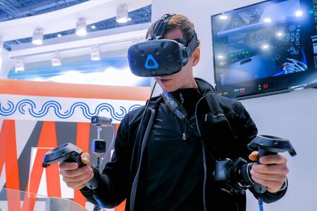 MOSCOW, RUSSIA - March 1, 2019: Virtual Reality Exhibition. Man using virtual reality headset and playing simulator of subway train operator. VR, augmented reality and entertainment conceptのeditorial素材