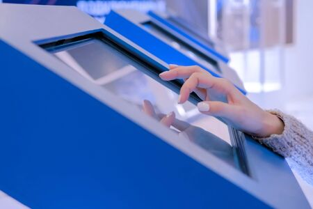 Education and technology concept - woman using interactive touchscreen display of electronic kiosk at technology exhibition or museumの写真素材