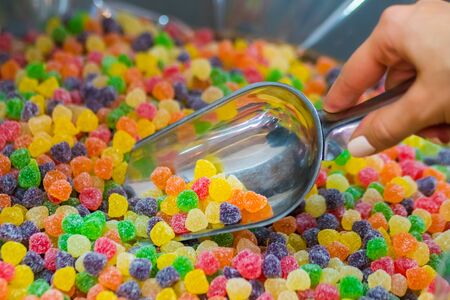 Woman hand with scoop taking colorful delicious marmalade jelly candies on counter of shop, grocery, market, cafe - close up view. Dessert, sale, sweet food and confectionery conceptの写真素材