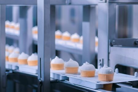 Icecream automatic production line - conveyor belt with ice cream cones at modern food processing factory. Food dairy industry, manufacturing, engineering and automated technology equipment conceptの写真素材