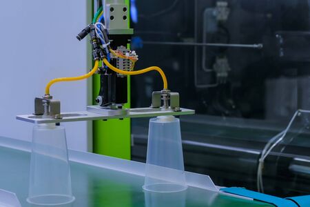 Automatic production line with robotic arm and moving polypropylene clear cups on conveyor belt of plastic injection molding machine at factory, exhibition. Manufacturing, industry, technology conceptの写真素材