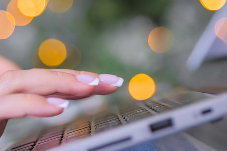 Woman hands typing on laptop computer keyboard - close up view. Christmas garland light bokeh...