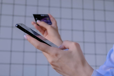 Woman using black smartphone mobile device, holding credit card, buying goods or ordering online -...
