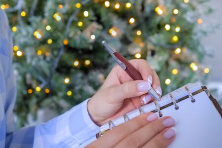 Woman writing to do list in vintage notebook organizer - close up view. Garland light illumination bokeh background. Christmas, motivation, management, productivity, planning, reminder, goals conceptの写真素材