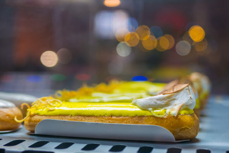 Assortment of delicious fresh cake eclairs with cream for sale on counter of shop, grocery, market,...