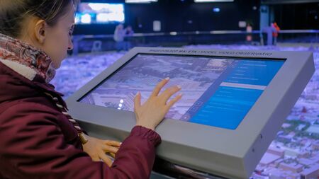 MOSCOW, RUSSIA - JUNE 05, 2019: Smart Expo. Woman using modern touchscreen display of electronic kiosk with interactive 3d architectural model of Moscow. Navigation, journey and technology conceptのeditorial素材