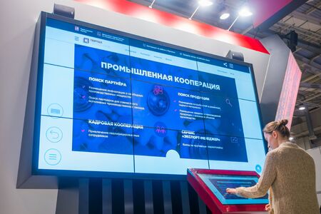 MOSCOW, RUSSIA - JUNE 05, 2019: Smart Expo. Woman using kiosk and watching presentation about Moscow industrial development on large interactive wall display at technology exhibitionのeditorial素材